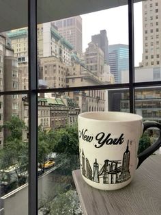 a coffee cup sitting on top of a window sill in front of a cityscape