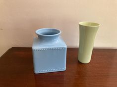 a blue vase sitting on top of a wooden table next to a green vase with beaded trim