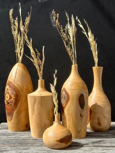 four wooden vases sitting on top of a table next to each other with dried plants in them