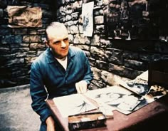 a man sitting at a table in front of a brick wall with pictures on it