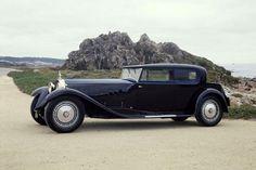 an old black car parked on the side of a road next to a rock formation