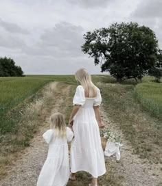 two women in white dresses walking down a dirt road