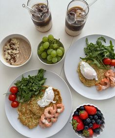 three white plates topped with food next to two glasses of water and some fruit on the table