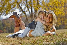 a mother and daughter laying on the grass in front of trees with their arms around each other