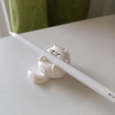 a white pencil sitting on top of a table next to a cat figurine