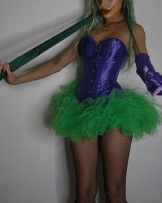 a woman dressed in green and purple holding an umbrella while standing next to a wall