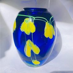 a blue glass vase with yellow flowers painted on the bottom and sides, sitting on a white surface