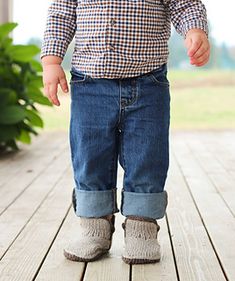 a toddler standing on a wooden deck with his hands in his pockets and wearing boots