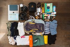 an assortment of personal items laid out on a wooden floor with water bottle and camera