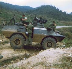 two men are riding on top of an army vehicle in the mountains with another man standing next to them