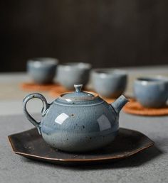 a blue tea pot sitting on top of a wooden plate next to cups and saucers