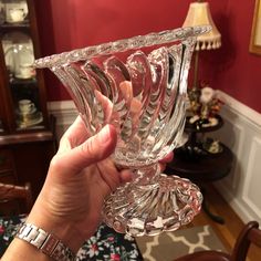 a person holding up a crystal wine glass in their hand with red walls behind them