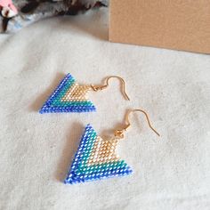 two pairs of beaded triangle earrings sitting on top of a table