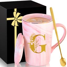 a pink marbled coffee mug next to a black box with gold lettering and a spoon