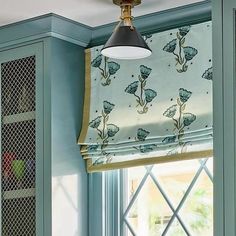 a kitchen with blue cabinets and green curtains on the window sill, along with a light fixture that is hanging from the ceiling