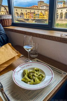 a bowl of food on top of a table next to a glass of wine