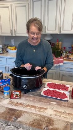 a woman standing in front of a crock pot filled with meatballs and vegetables