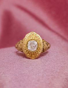 a gold ring with a white diamond in the center on a pink velvet cloth background