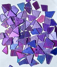 a pile of purple and blue glass mosaics on a white table top with water droplets all over the surface