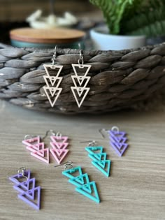 three pairs of earrings sitting on top of a wooden table next to a basket and potted plant