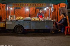 two people sitting at a food cart in front of an orange tent with red curtains