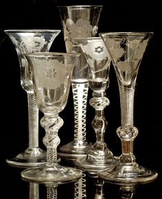 five glass goblets sitting on top of each other in front of a black background