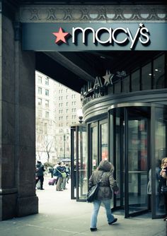 a woman walking down the sidewalk in front of macy's store with her coat on