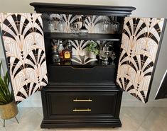 an art deco display cabinet with wine glasses and liquor bottles on the top, next to a potted plant