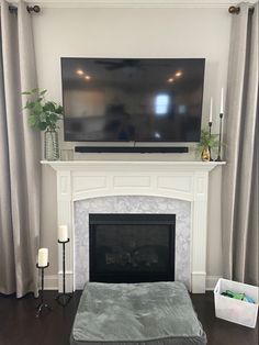 a flat screen tv mounted above a fireplace in a living room with curtains on the windows