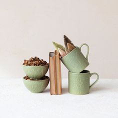 three green mugs filled with food next to an open book