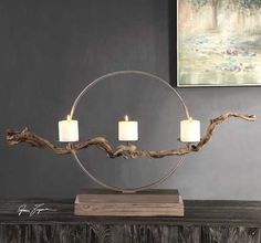 three candles are lit in front of a circular metal candle holder on top of a wooden table