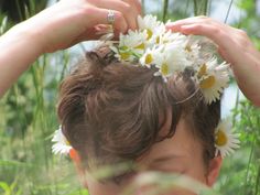 a woman holding flowers in her hair while standing next to tall grass and plants with one hand on top of the man's head