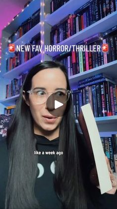 a woman with long hair and glasses holding a book in front of bookshelves