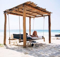 a woman laying in a hammock on the beach under a wooden pergol