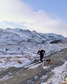 a man running in the snow with his dog on a path next to some mountains