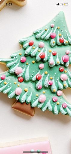 a decorated christmas tree cookie next to some cookies on a white table with pink and green icing