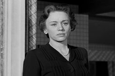 black and white photo of woman in dress standing by column with pearls on her necklace