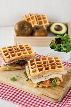 two waffle sandwiches sitting on top of a cutting board next to an avocado