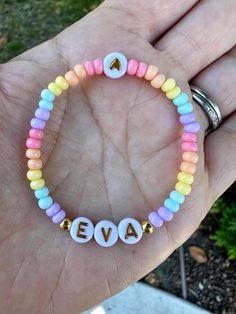 a hand holding a bracelet with the word eva spelled out in small letters on it