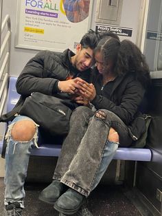 a man and woman sitting on a train looking at their cell phones while they both look down