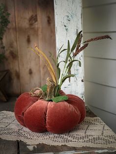 a red pumpkin sitting on top of a piece of cloth next to a wooden wall