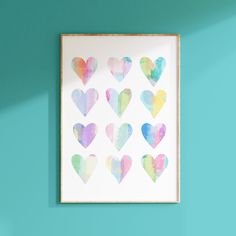 watercolor hearts are arranged in the shape of heart shapes on a white frame against a teal wall