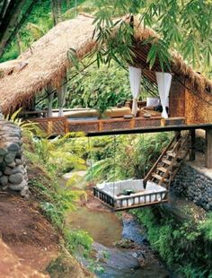 a house built over a small stream in the jungle with thatched roof and steps leading up to it