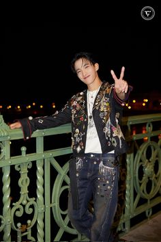 a young man standing on top of a balcony next to a green railing with his hand in the air