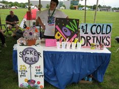 a man standing next to a table covered in signs and flowers at an outdoor event