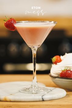 a pink drink with strawberries on the rim in front of a bowl of whipped cream