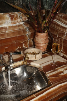 a sink and some wine glasses on a counter with brown marble walls in the background