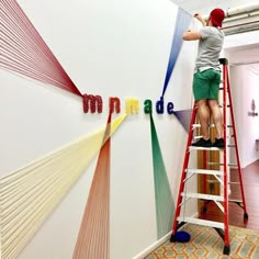 a man standing on a ladder painting the word made out of strips of colored yarn