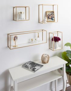 three gold framed pictures hang on the wall above a white table with a magazine and vase