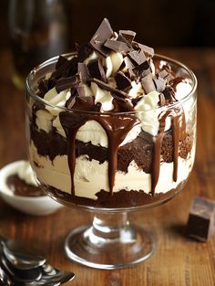 a dessert dish with chocolate and cream toppings on a wooden table next to silverware